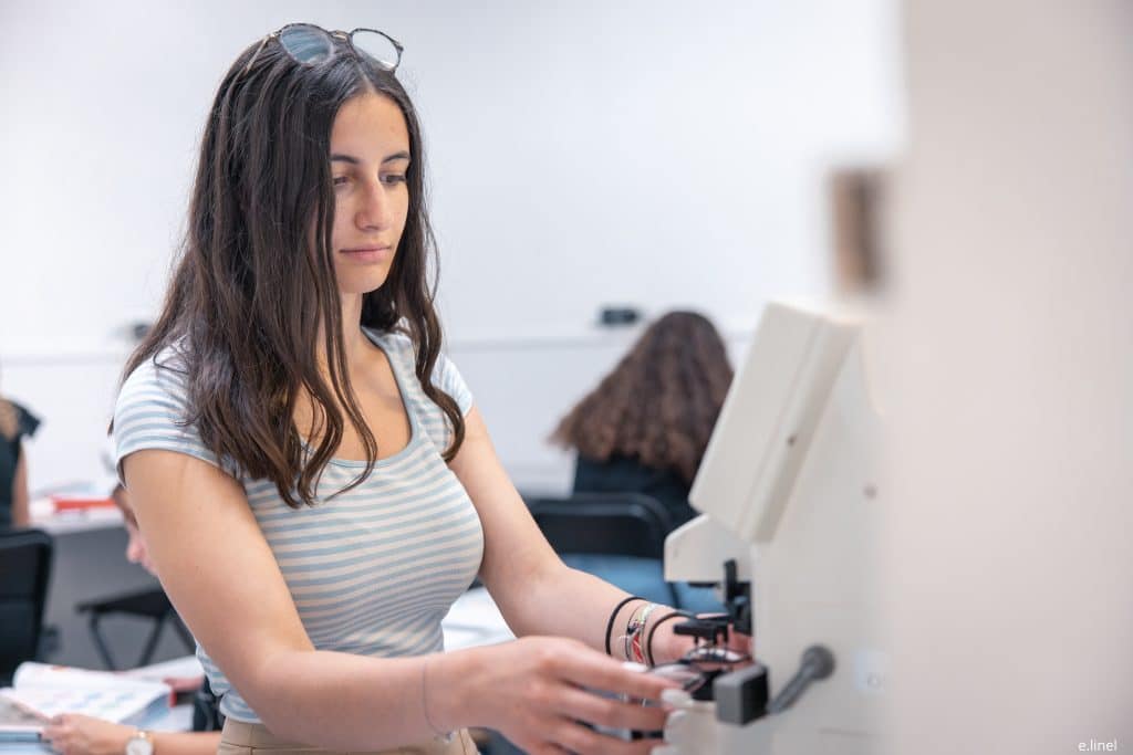 Jeune fille manipulant une meuleuse dans une école d'optique à Paris afin de représenter le salaire des opticiens titulaires d'un BTS : perspectives et évolutions de carrière